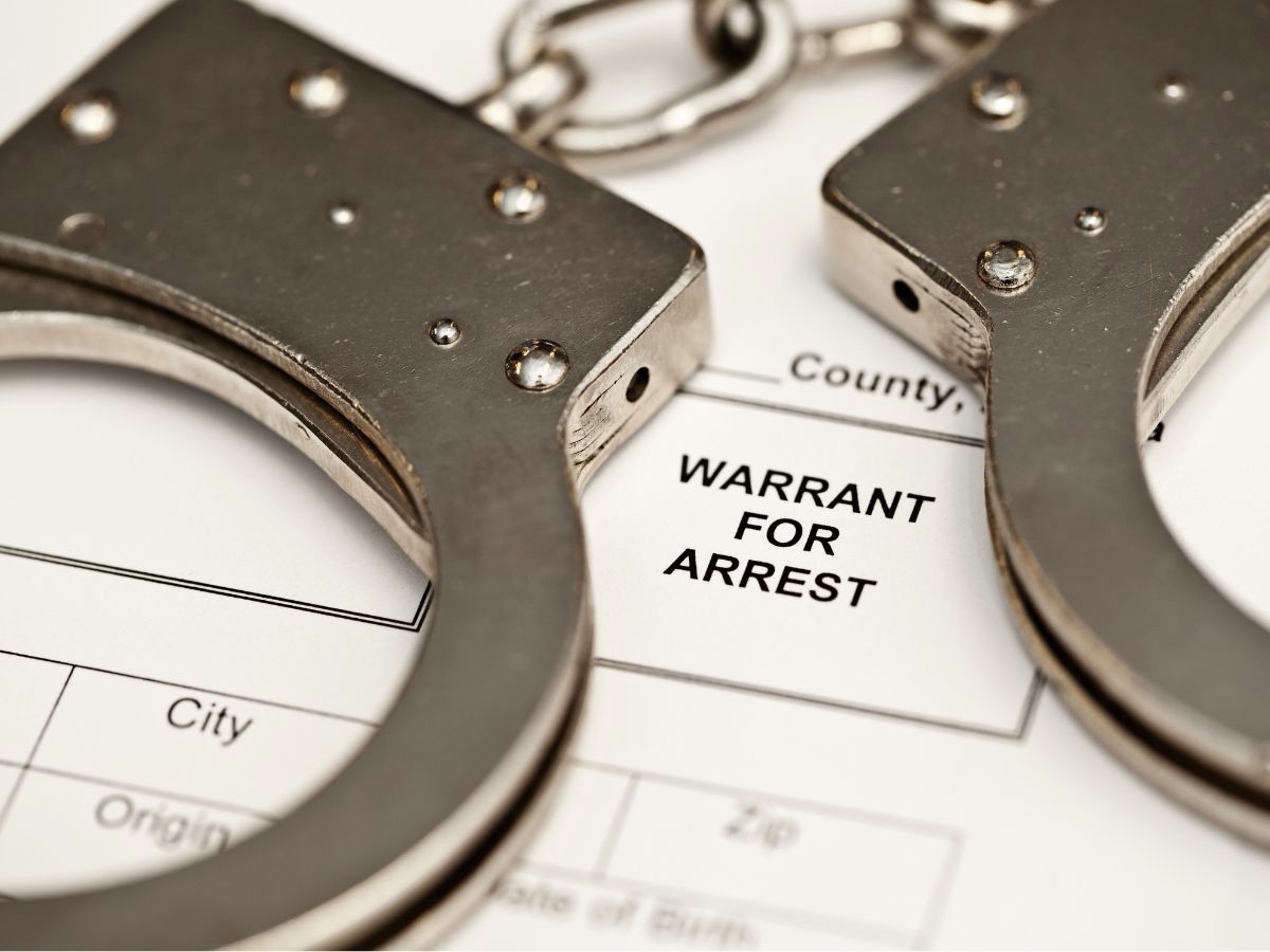 Pair of Handcuffs on Top of a Paper Which Reads 'Warrant for Arrest'