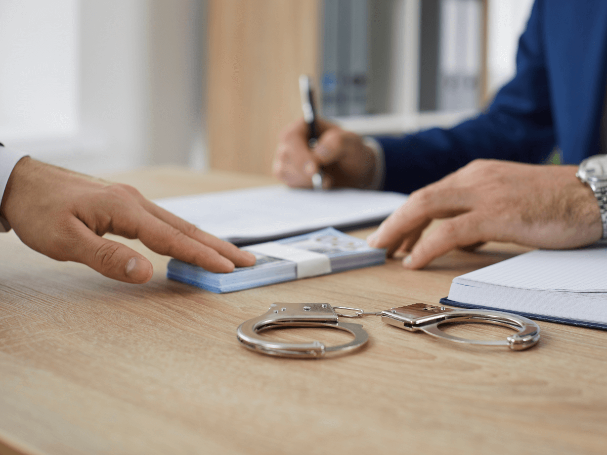 Money on the table with handcuffs and an agreement being written.