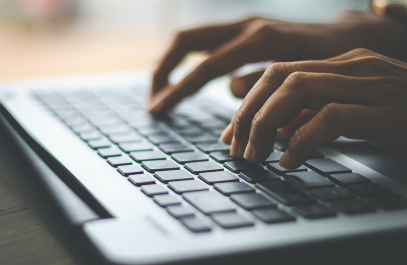 Close-up of hands typing on a laptop keyboard.