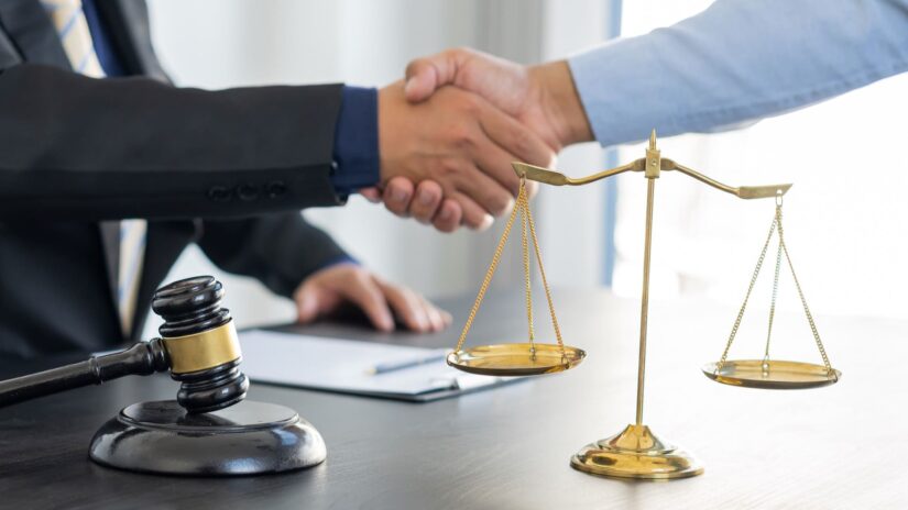 Two persons shaking hands in front of gavel and scale
